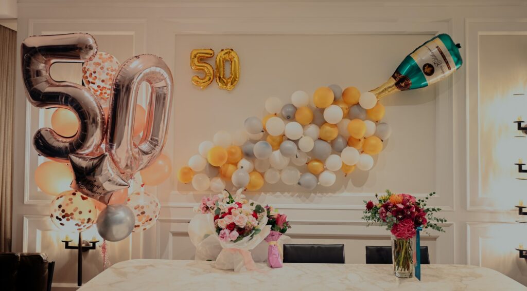 A perfect birthday decoration filled with 3 bouquets of flowers and a glass vase full of flowers. With balloons in the background with a 50 numbered balloon
