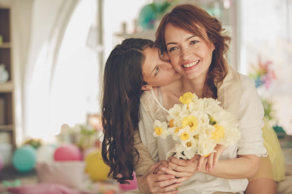 A Girl kissing a woman with a daffodils bunch