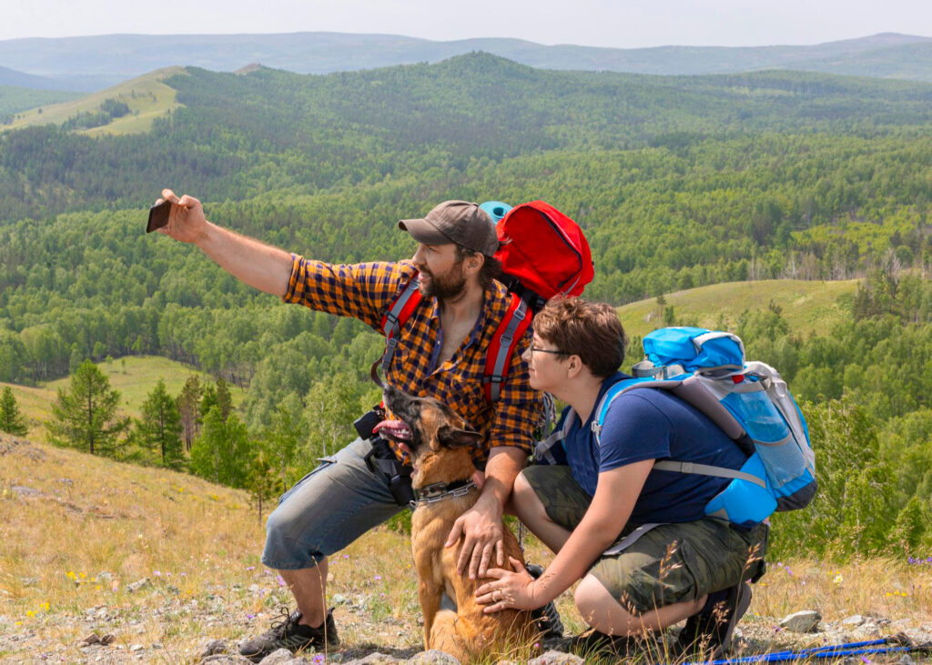A Man with a Child and a Dog Taking Selfie on a Mountain