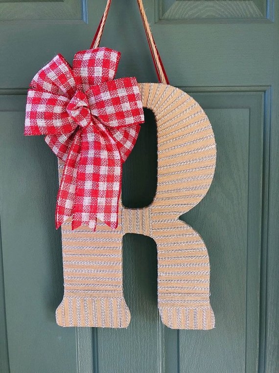 A letter monogram wrapped in yarn and a ribbon attached to the top, hung from a door