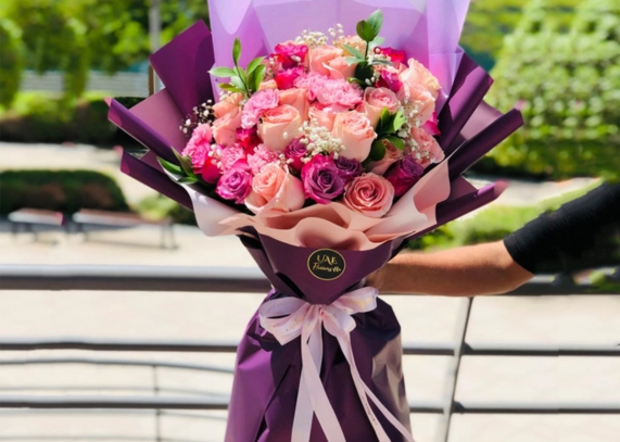 A woman is holding a bouquet of pink and purple roses, perfect for Christmas gifts for family.
