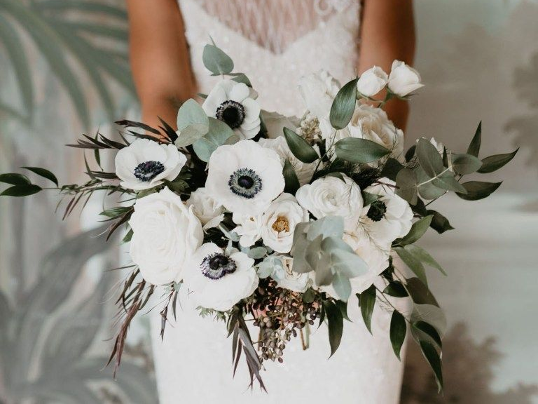A bride holds a bouquet of popular wedding flowers: white anemones and eucalyptus.