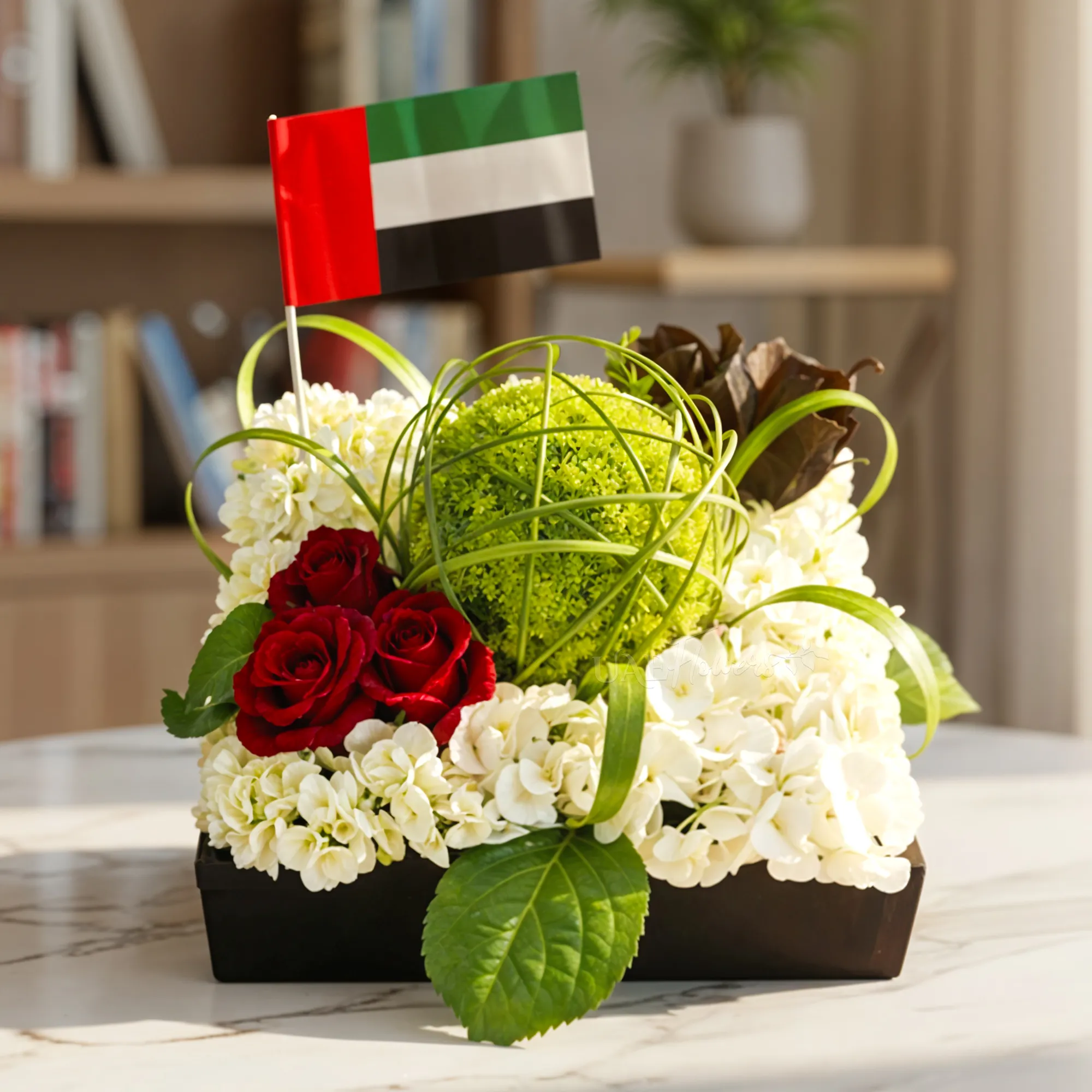 UAE National Day floral arrangement featuring red roses, white flowers, green foliage, and a UAE flag in a premium gift box.