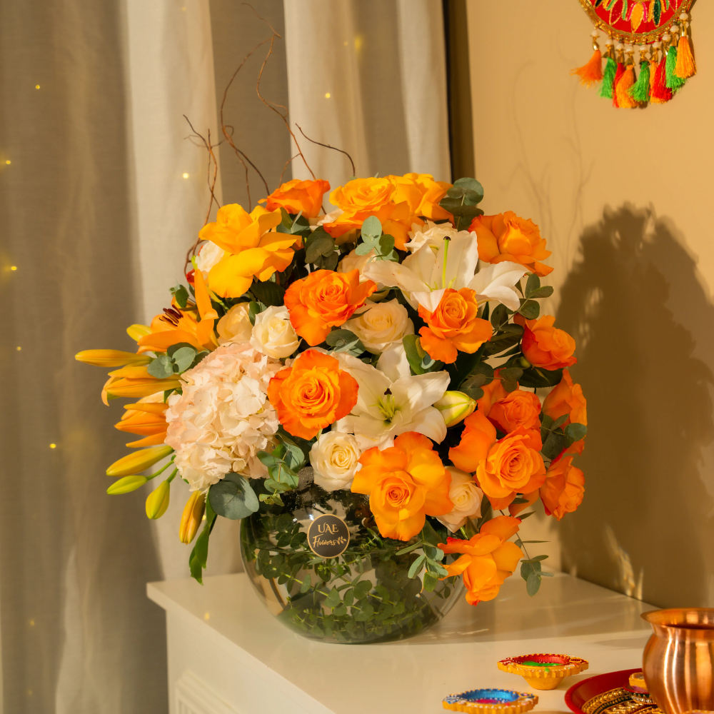 Corporate Diwali Gifts Online featuring orange roses, white lilies and cream hydrangeas in an elegant glass vase with greenery and festive Diwali décor.